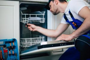 a male in overalls doing dishwasher maintenance